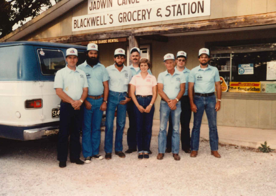 Darrel (far left) with his staff An older image from the 70s or 80s. A group of 7 men and a woman stand before the Jadwin Canoe Rental building. They all wear light blue shirts and blue jeans, apart from the lady, who wears a pink shirt. The men all wear trucker-style hats. A small van c