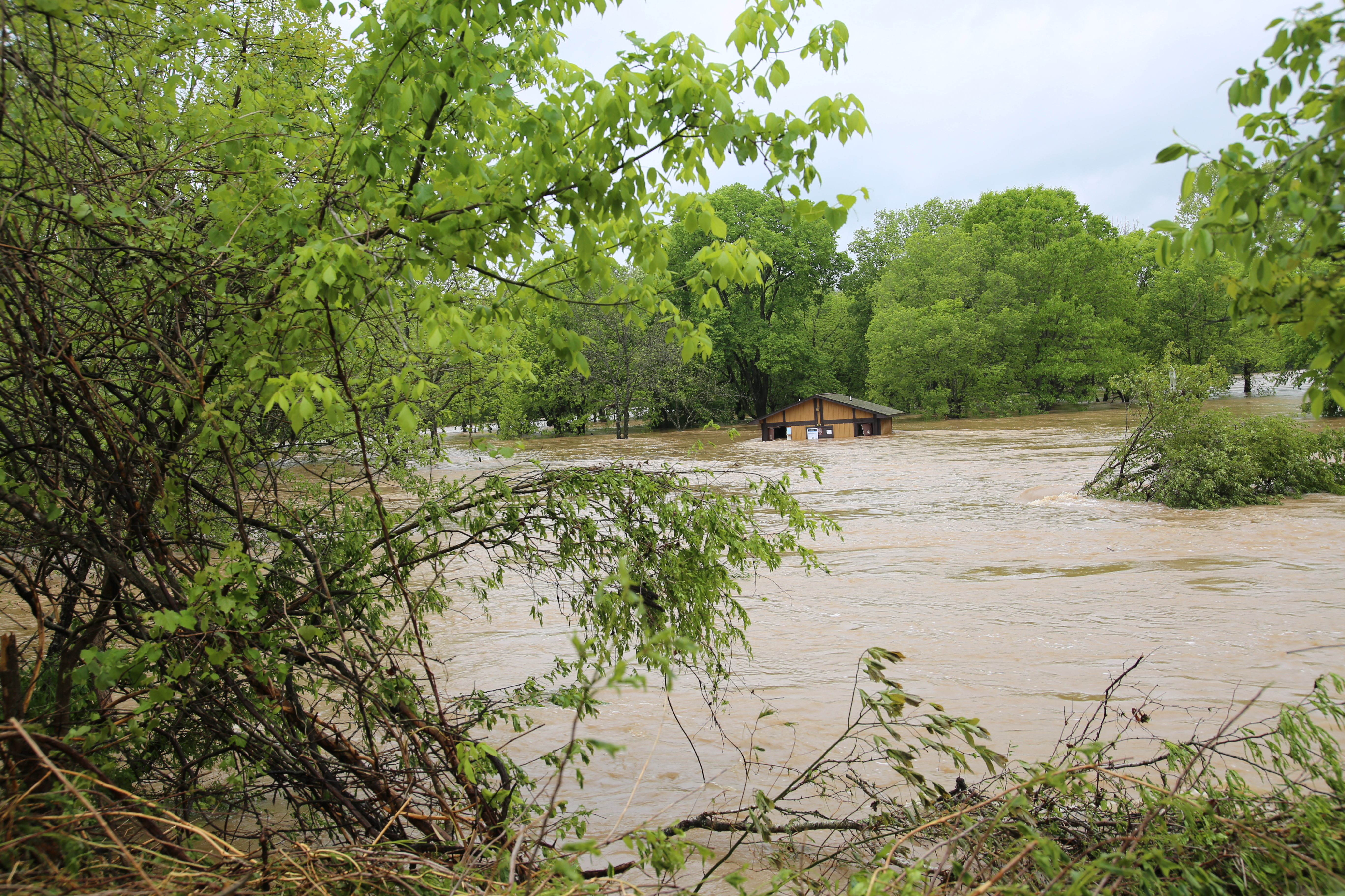 A flooded campground with brown water. A brown bathroom building is halfway under water.