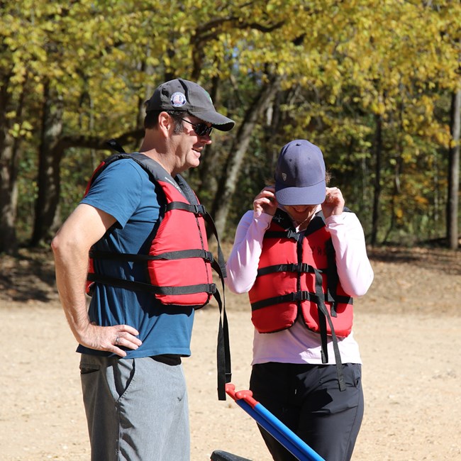 Two people stand on a gravel bar wearing sunglasses and PFDs.