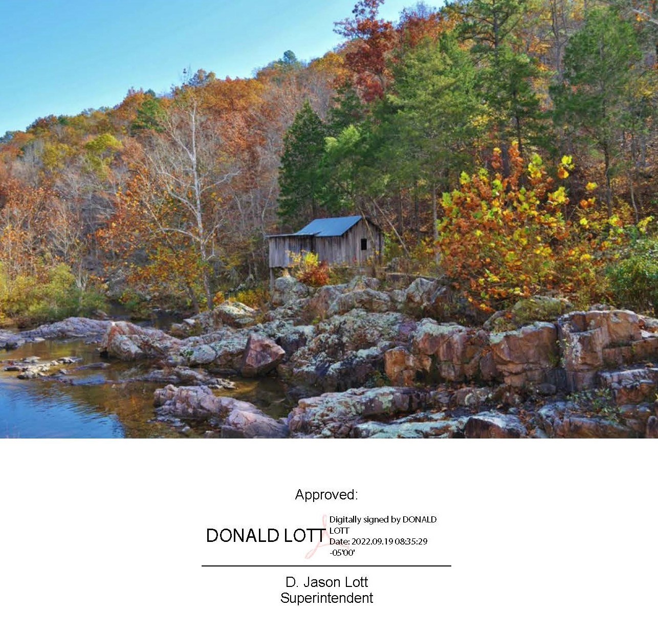 A picture of Klepzig Mill, an old wooden mill sits on a small bluff overlooking a creek surrounded by fall foliage. Text is the signature of the Park Superintendent Jason Lott on September 19, 2022.