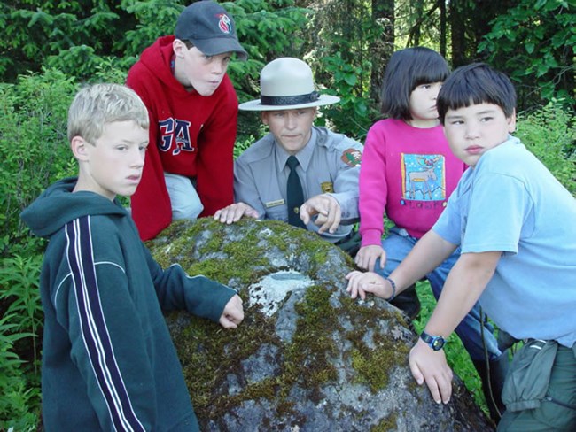 Ranger with flat hat talking with children by boulder Ranger with flat hat talking with children by boulder