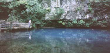 man on platform overlooking blue spring