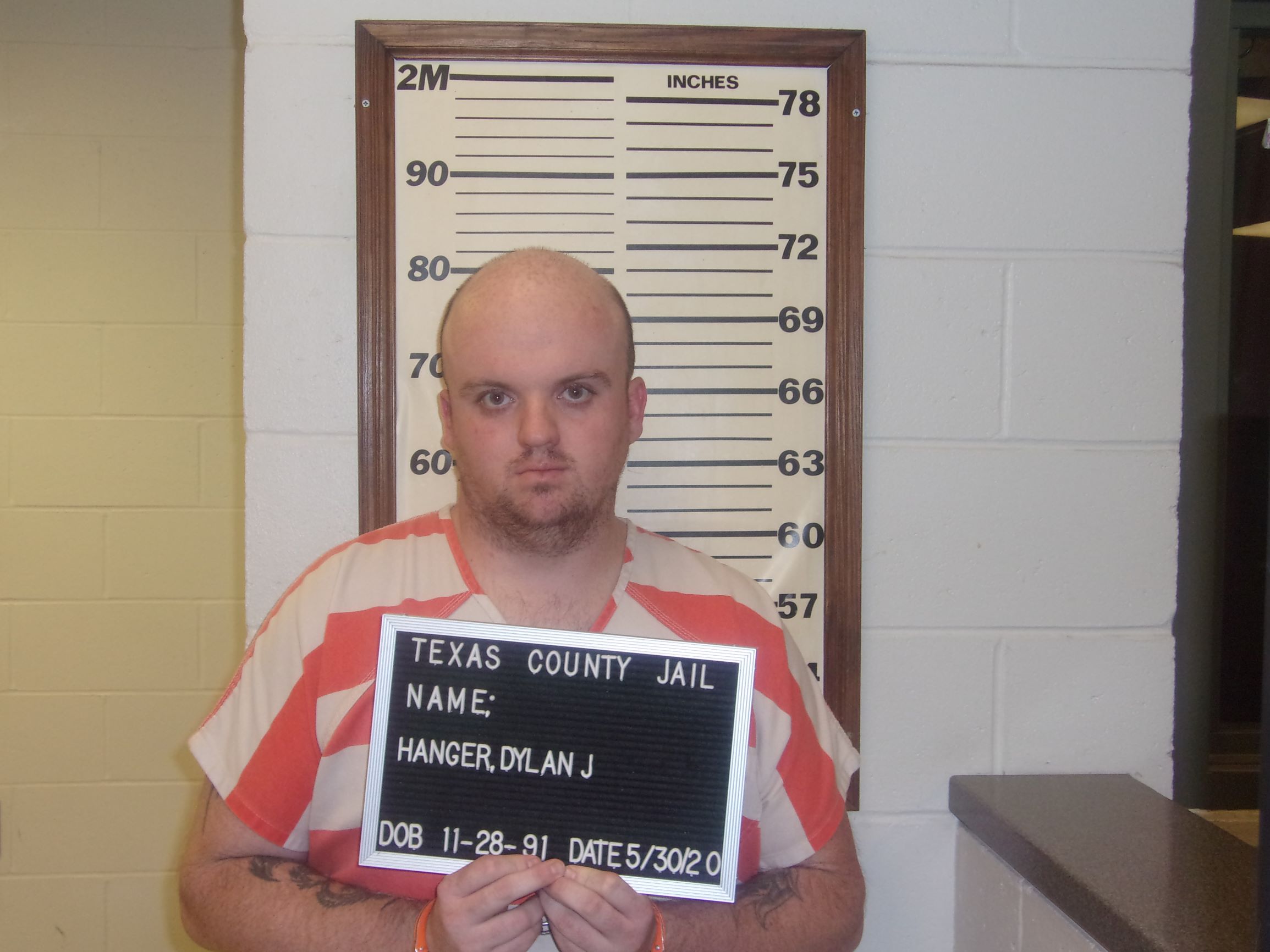 picture of Dylan J. Hanger in striped inmate uniform holding sign by measuring wall