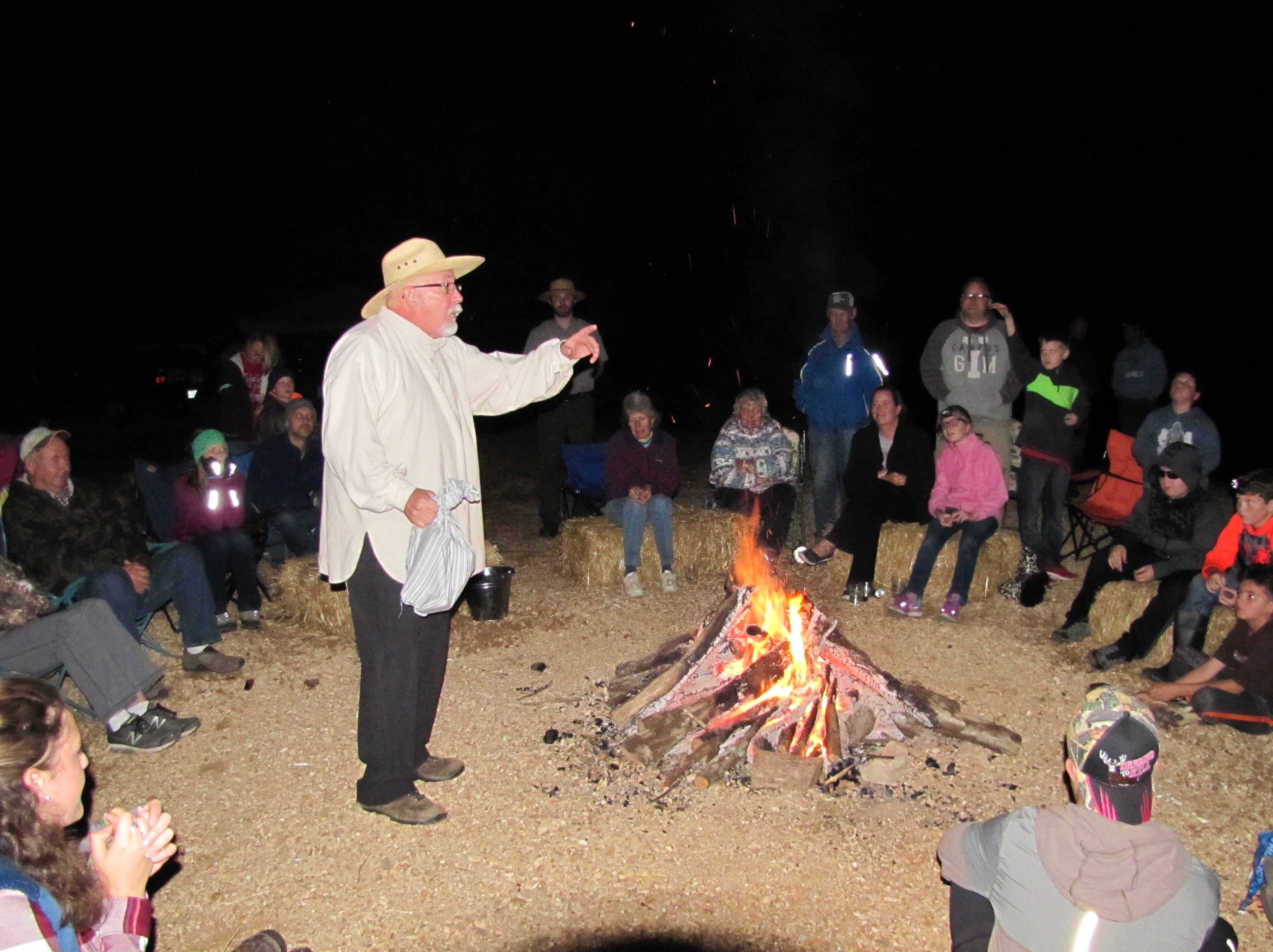 a storyteller by a fire at night with a crowd on straw bales