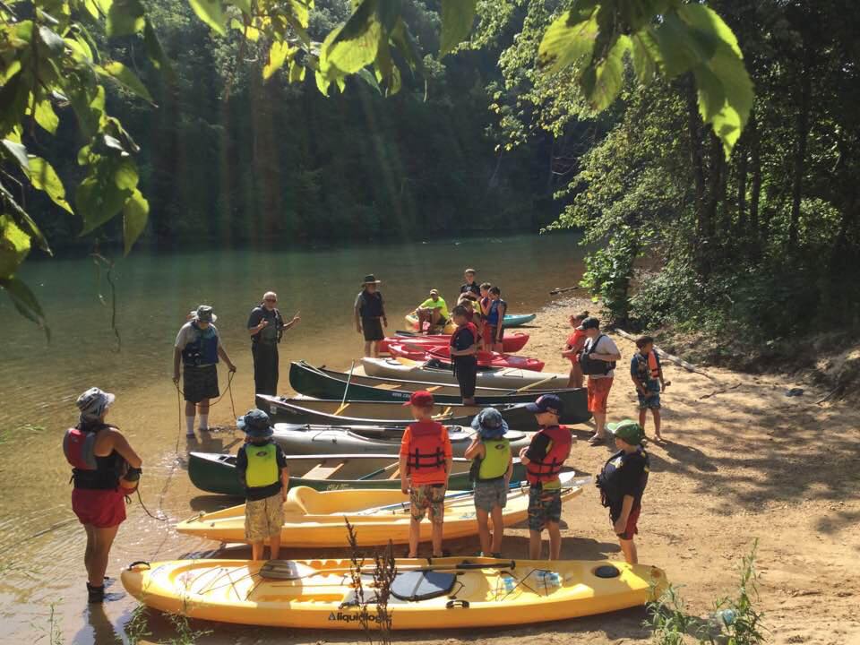 youth on river bank by kayaks and river in background