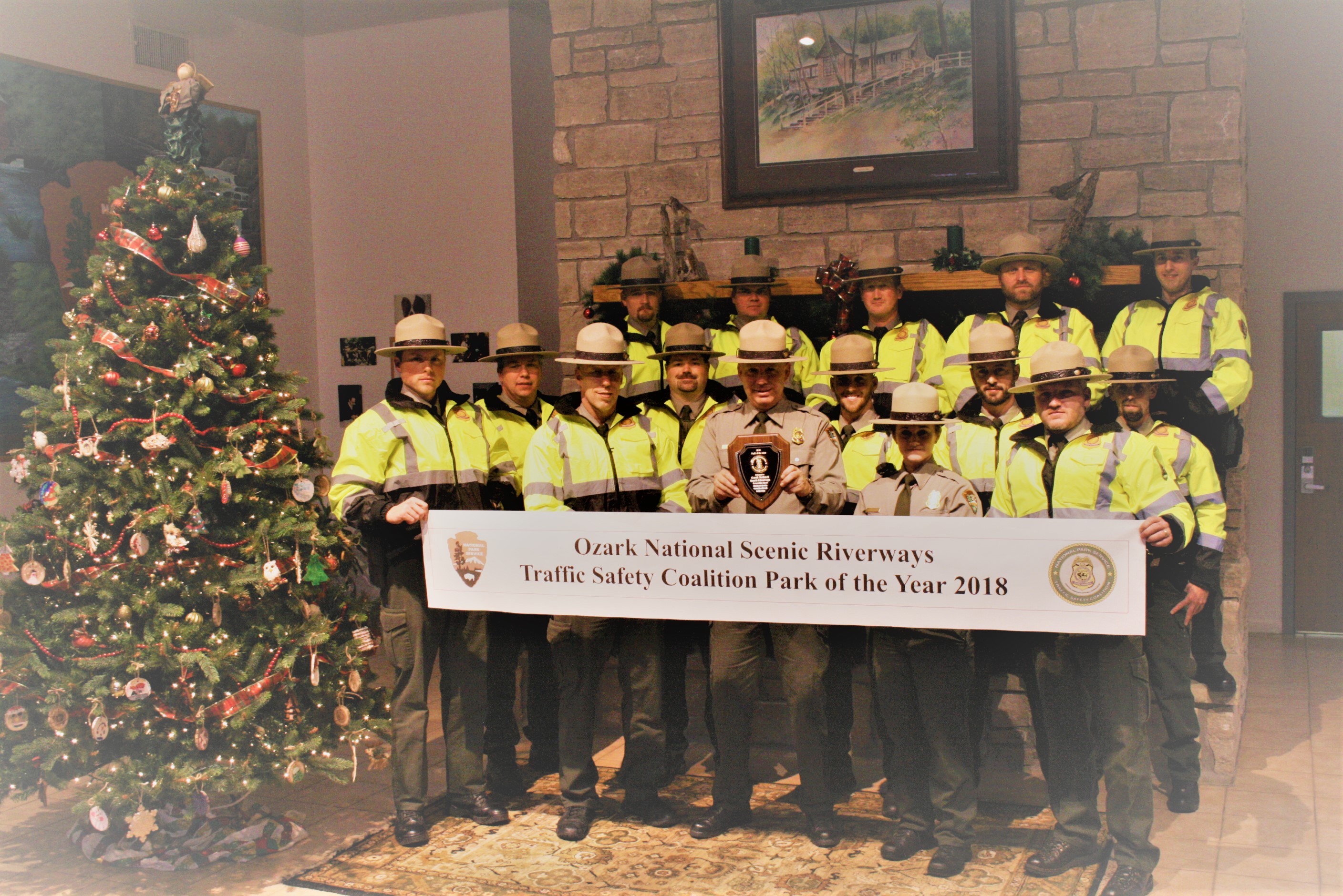 group of law enforcement rangers holding banner by christmas tree in uniform and yellow safety vest