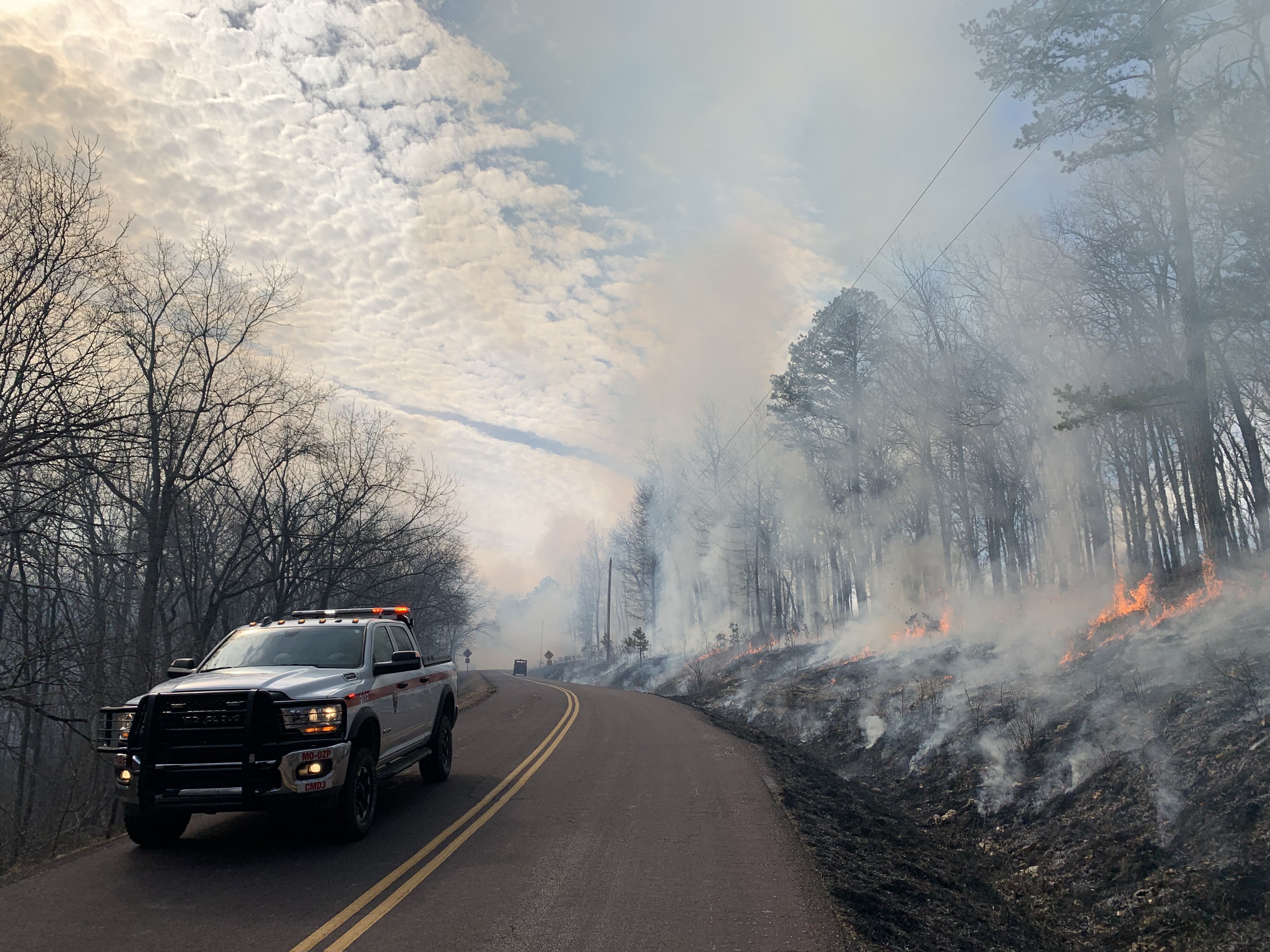 Prescribed fire road A national park service fire truck in country 2-lane highway with a smokey forest scene just off the road.
