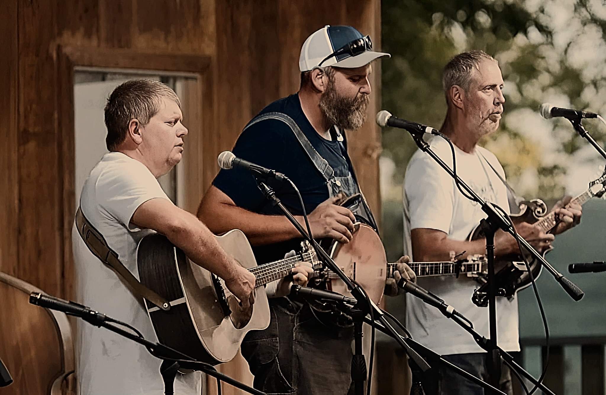 3 men during a bluegrass festival on stage playing guitar, banjo and mandolin
