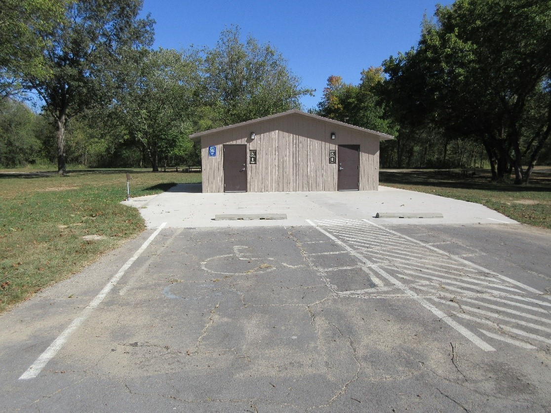 a grey stone park restroom with handicap parking sign in front