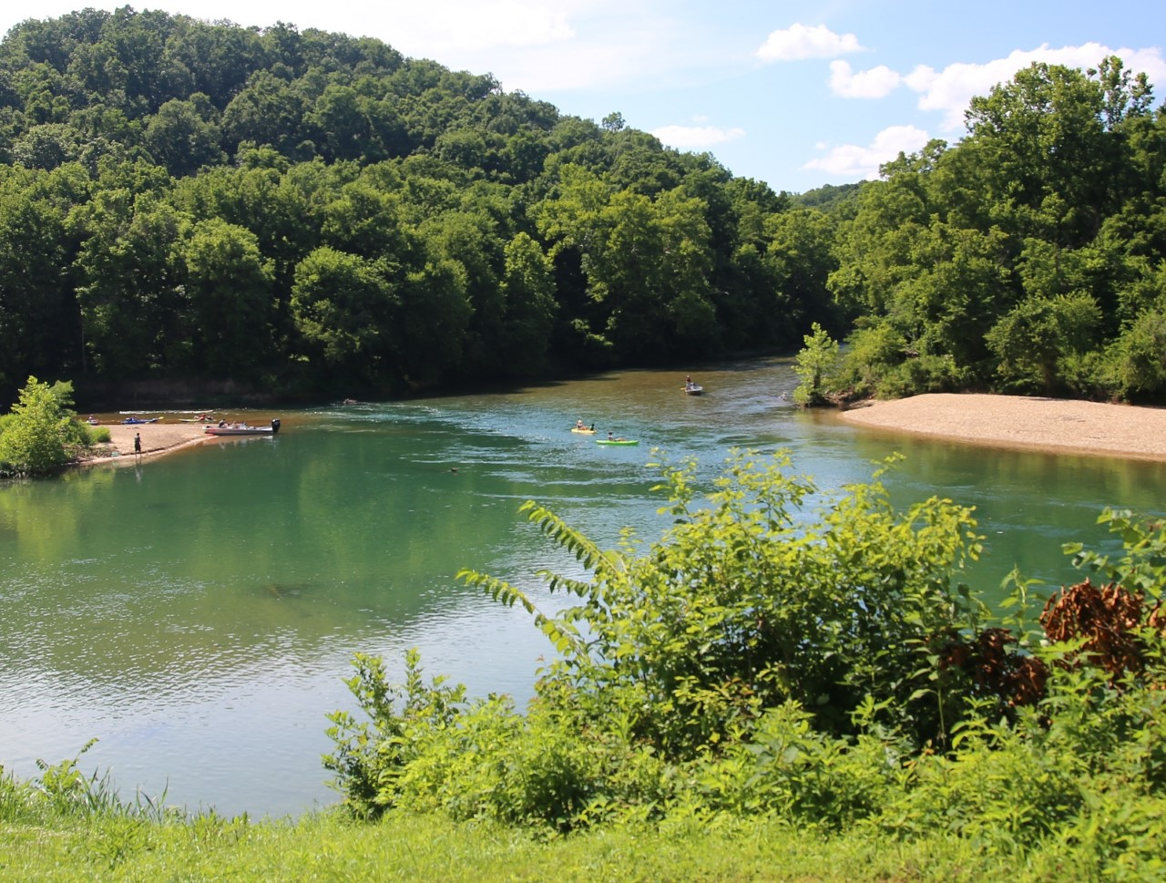 downloadxx0asa A river scene with rolling hills and gravel bars. kayaks and john boats are in the river.