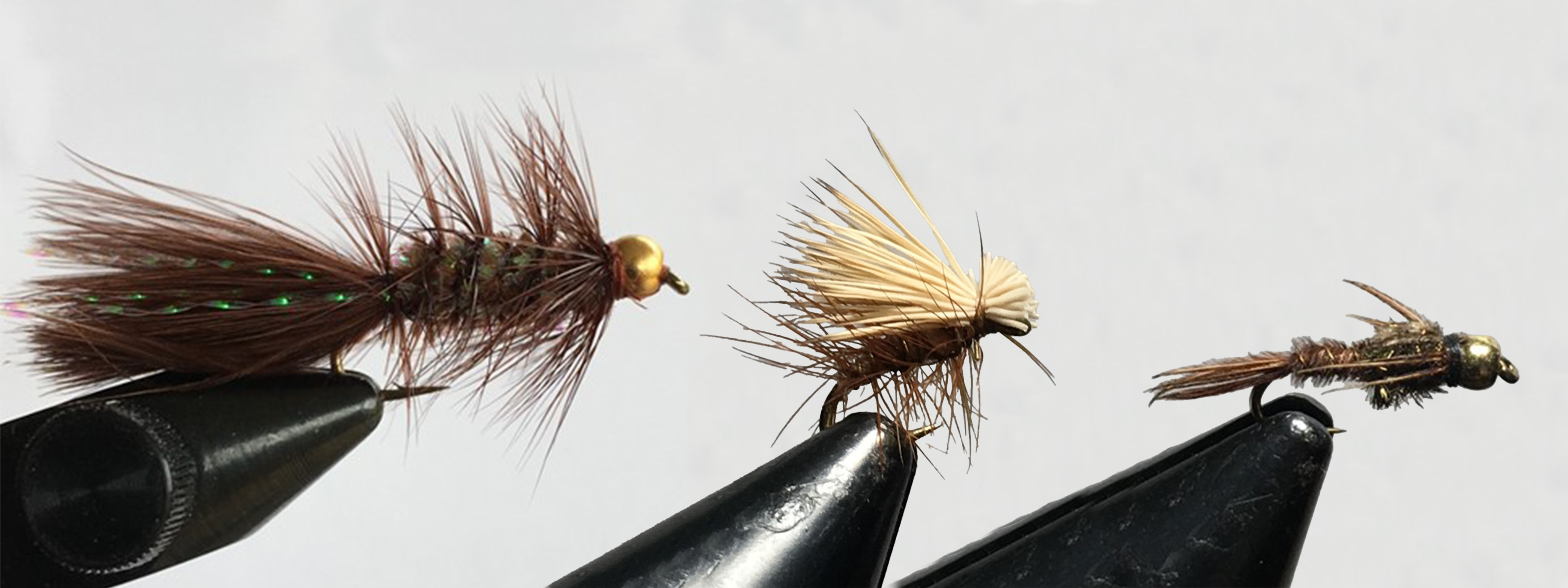 OZAR_flyTyingSamples_markVanPatten Three hand-tied fly fishing flies sit on display. They vary in size and fluffiness.