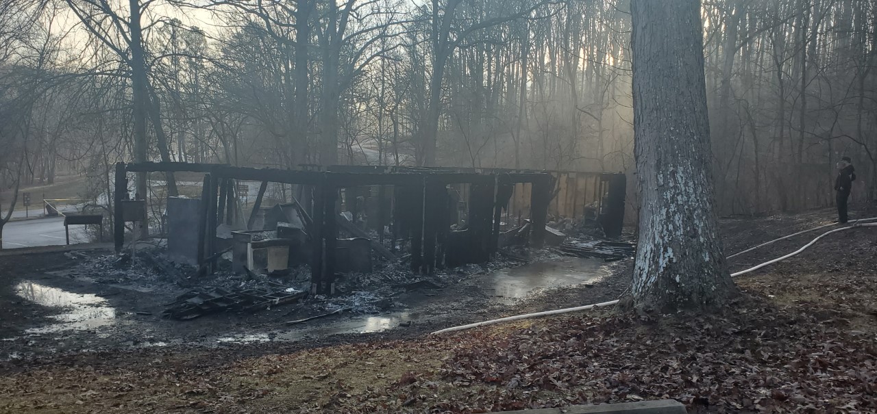 Round Spring ranger station charred from fire and smoldering and an investigator looking toward the scene.