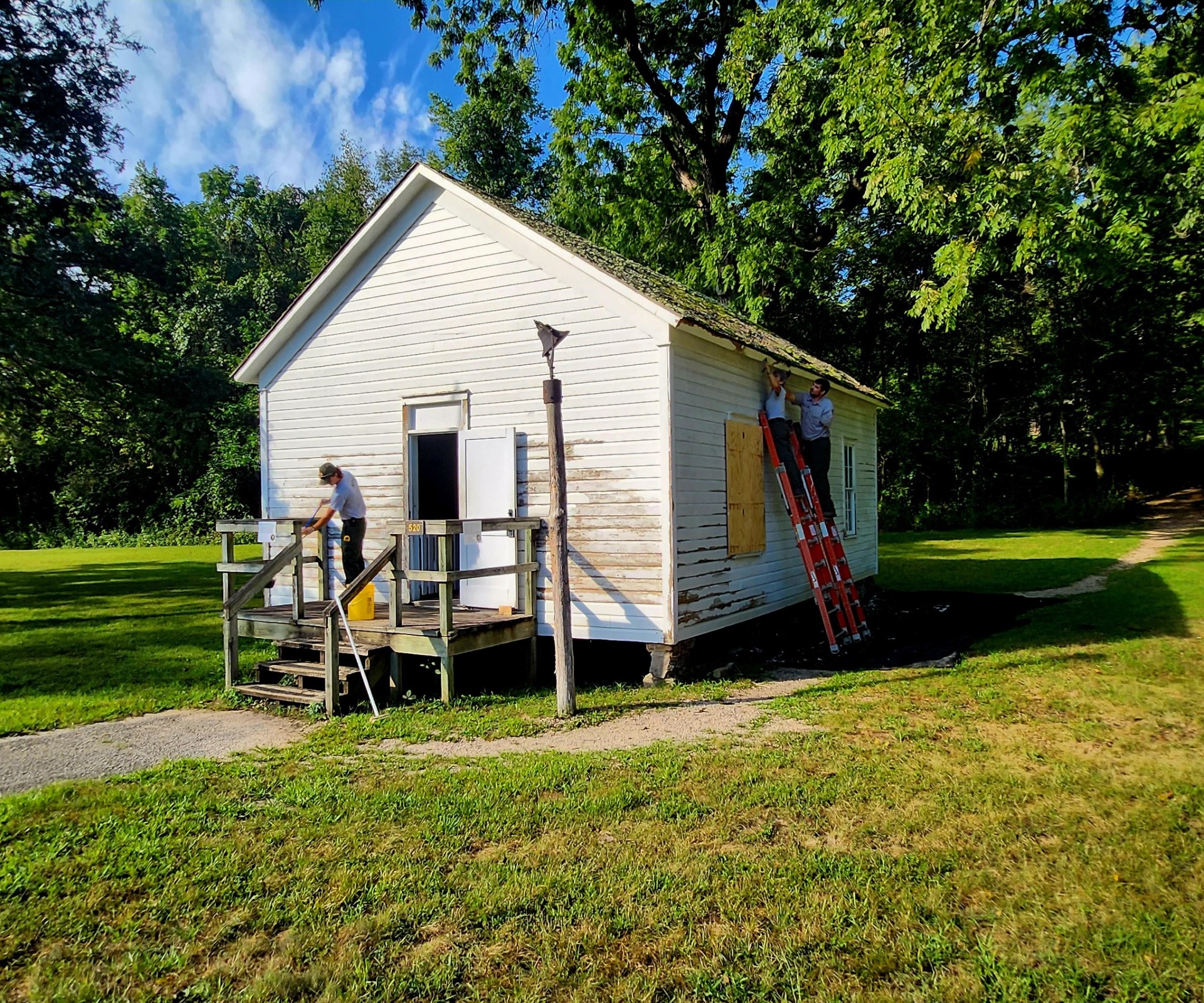 thumbnail_370192177_686983983458711_8660570216951489252_n A National Park Serivice maintenance member sweeps the porch of the Storys Creek School. Visible spots where the paint has been scraped off is present.