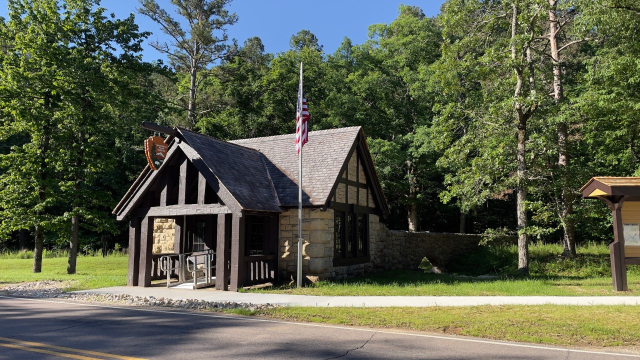 A small wooden beam and light cut stone structure from the state park era of the 1930's. A park arrowhead and U.S. flag adorn the structure.