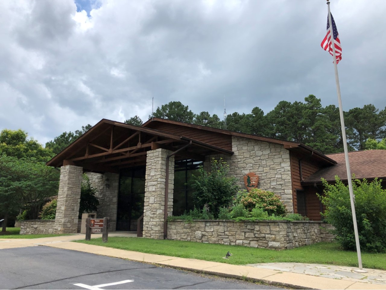 Park headquarters building, stone structure with wooden beams, NPS arrowhead on side of building, flag pole with flag out front of the building