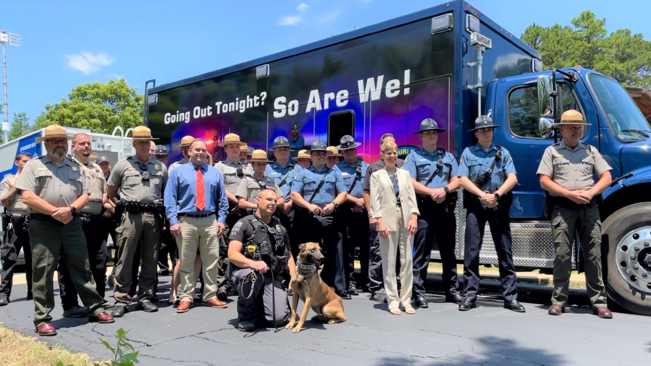 A group of law enforcement officers stand next to a large box truck style vehicle that says "Going out tonight?, so are we!"