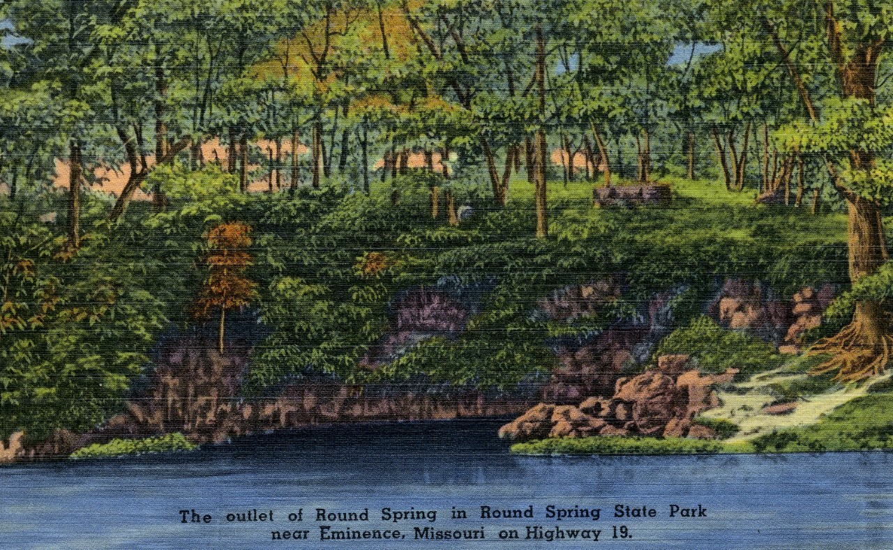 A historic color postcard showing round spring and rocks surrounding, text reads the outlet of round spring in round spring state park near Eminence, Missouri on Highway 19