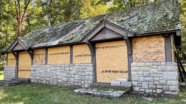 A double entry stone and wood structure with plywood over windows and doors.