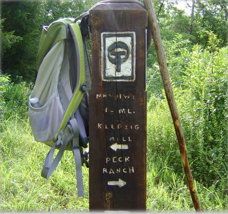 A hikers gear rest against an Ozark Trail directional post
