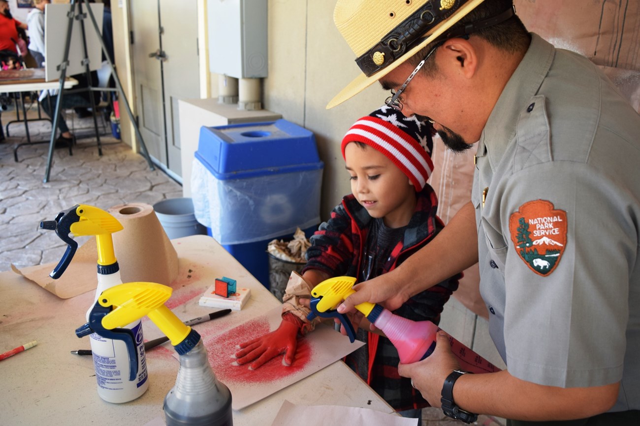 A Ranger helps a boy with a cave art activity