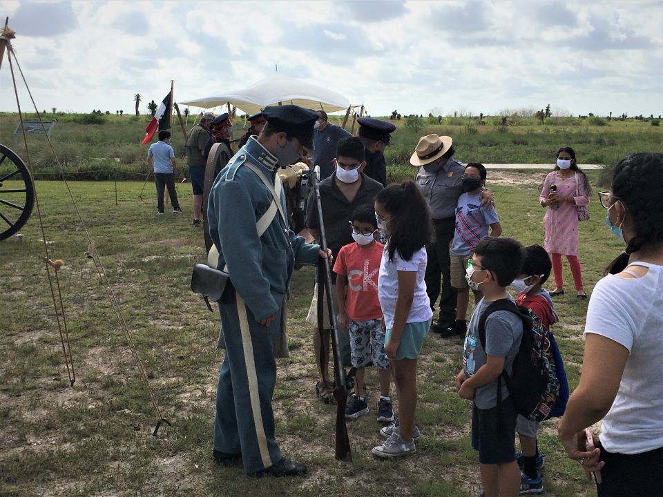 Visitors at an outdoor program talking to a volunteer in a Mexican War era infantry uniform.