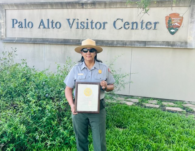 Superintendent Oralia Fernandez stands in front of building holding her years of service plaque.