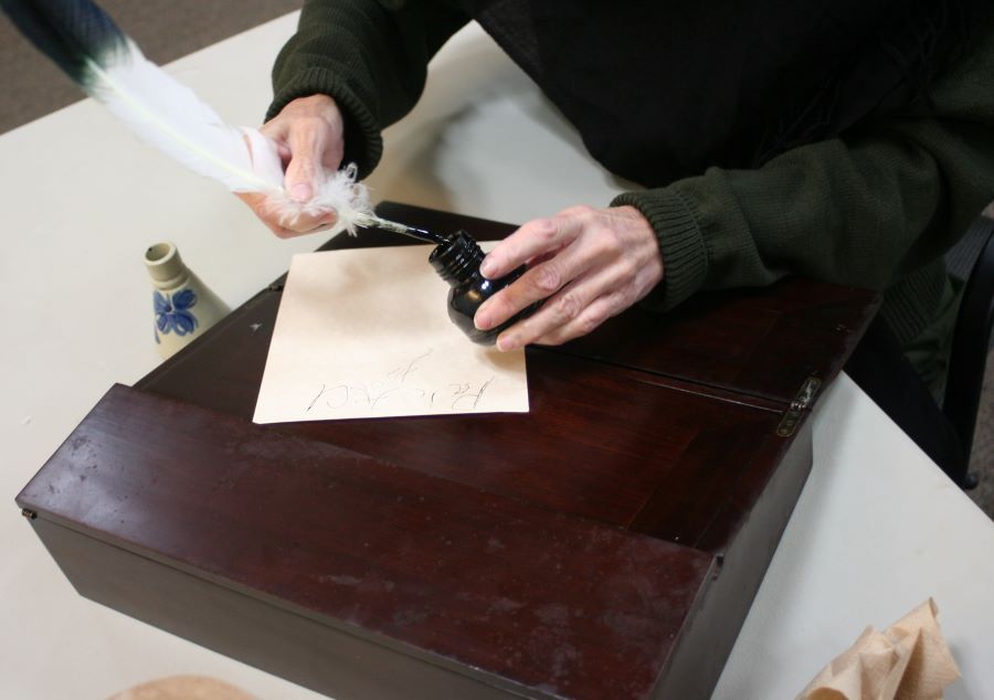 A person writing on paper with a quill pen