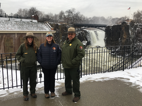 Two NPS Rangers and a Stewards Intern are standing in front of a the snowy Great Falls. Rangers in front of the Falls
