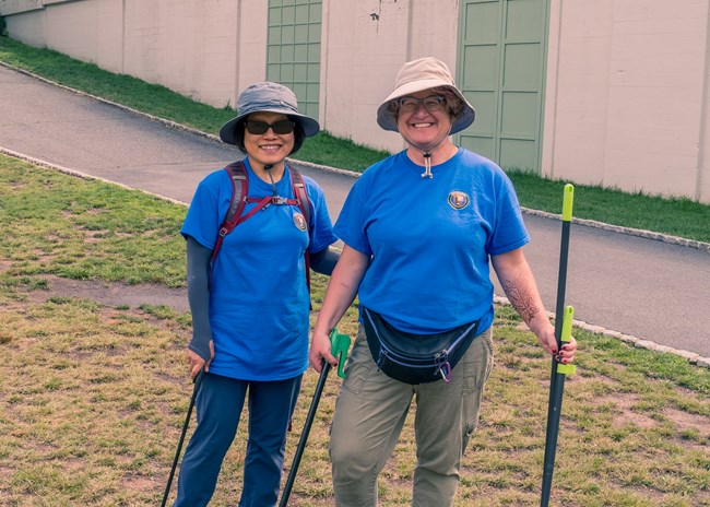 Two women in blue park service volunteer shirts, holding garbage pickers