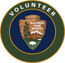Green circular logo with gold lining reading "Volunteer" with a National Park Service arrowhead on a center field of blue