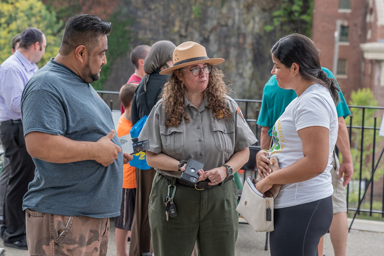A park ranger provides information to two visitors on either side of her