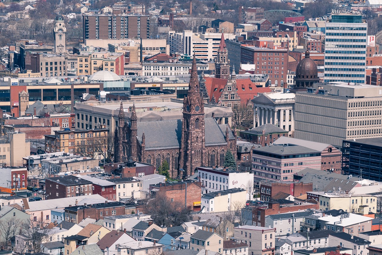 Aerial view of Paterson's "Little Dublin" neighborhood, looking past two & three-story buildings to the Cathedral of St. John the Baptist & the tall buildings of downtown