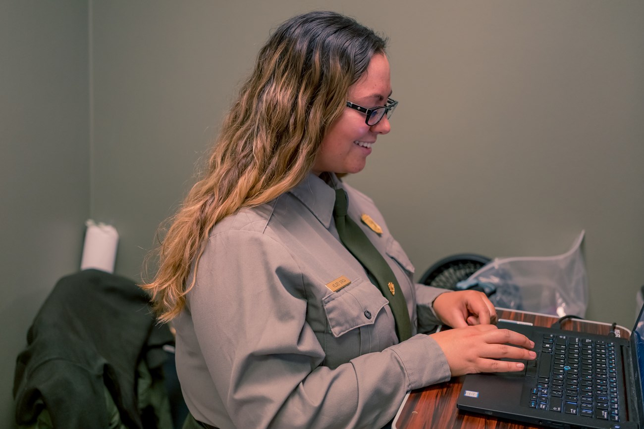 A park ranger smiles as she works on a laptop computer
