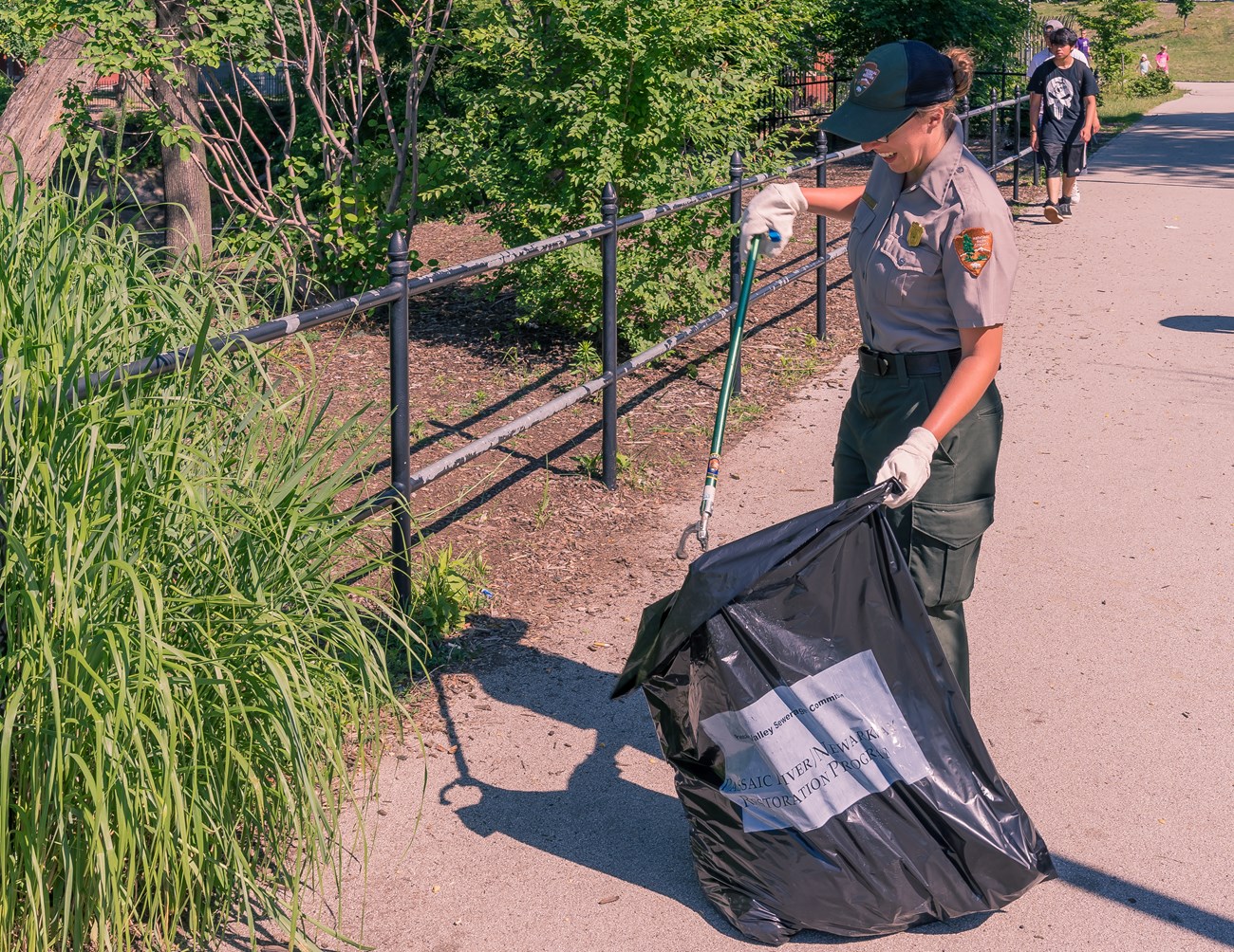 A park ranger in maintenance clothing smiles as she collects trash with a picker