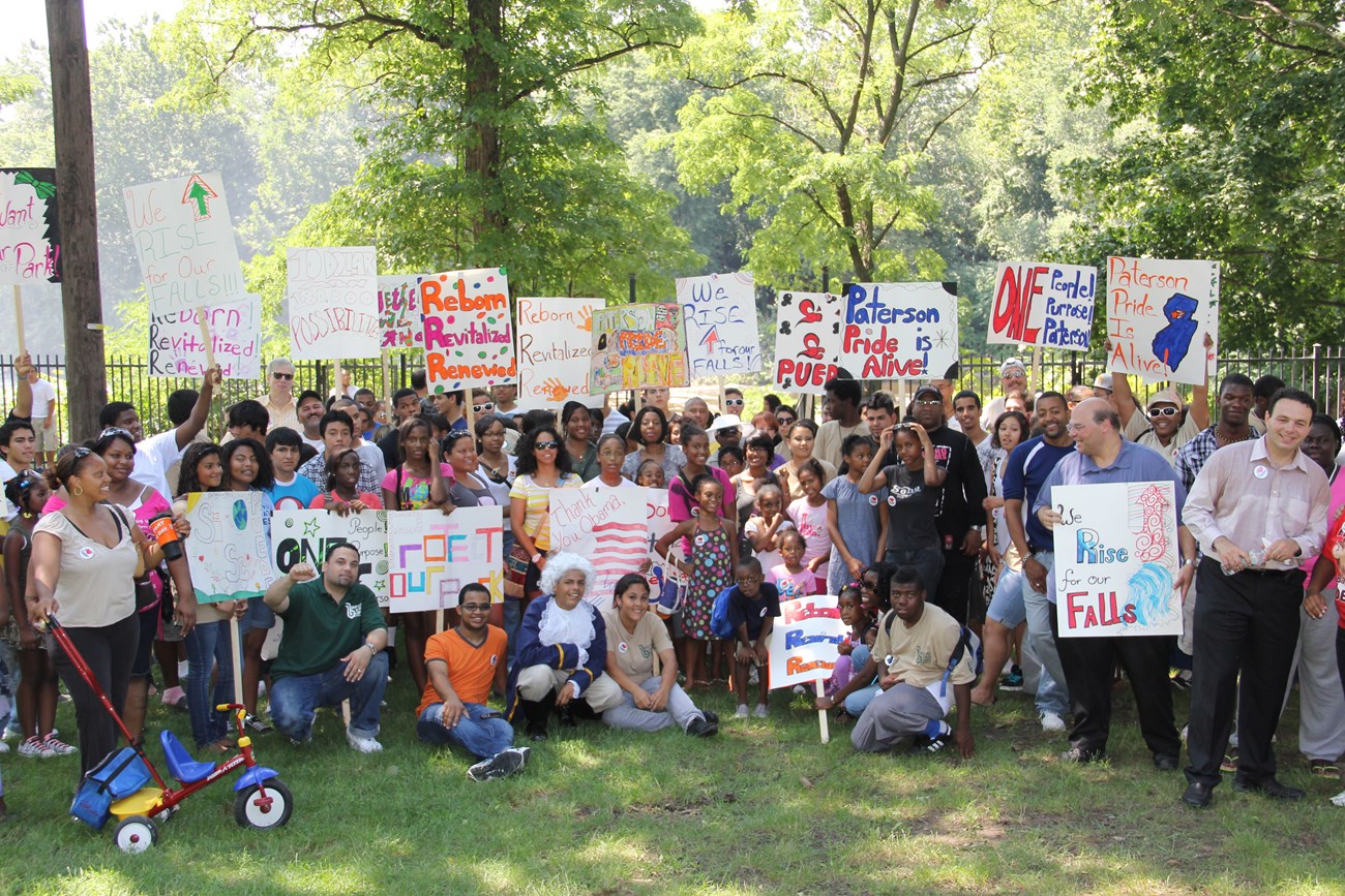 A crowd of people, largely youths, hold signs in support of Paterson and Paterson Great Falls