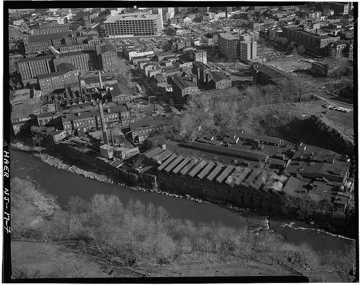 1983 aerial view of large, tightly packed brick factories lining the Passaic River