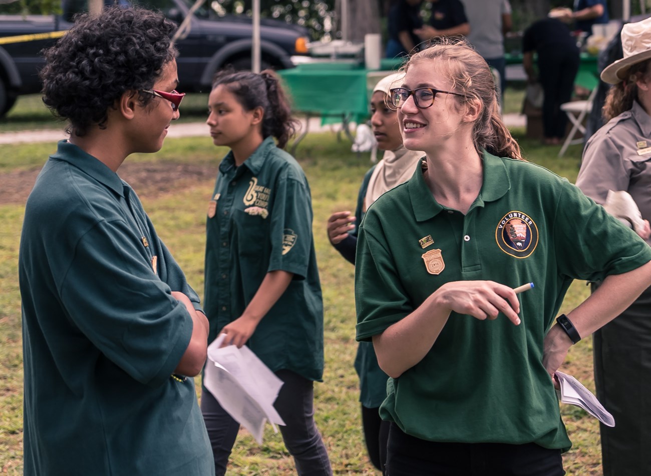 Green shirted volunteers & Great Falls Youth Corps members smile as they collaborate at an event at Paterson Great Falls National Historical Park