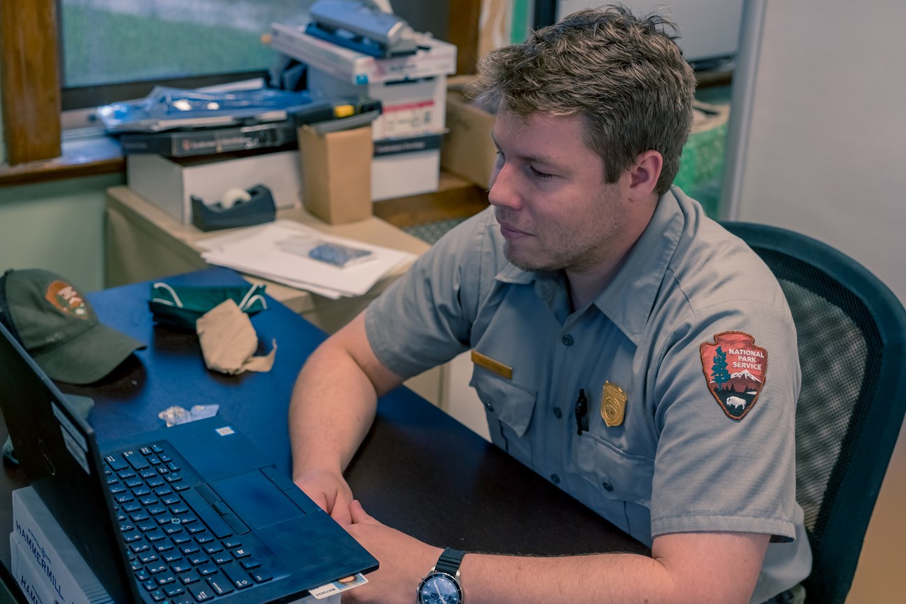 A park ranger sits at a laptop computer in an office