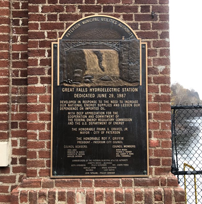 Plaque for the rededication of the Great Falls Hydroelectric Station on June 29th, 1987, w/ a list of local officials, a rendering of the falls, & the Paterson Municipal Utilities Authority