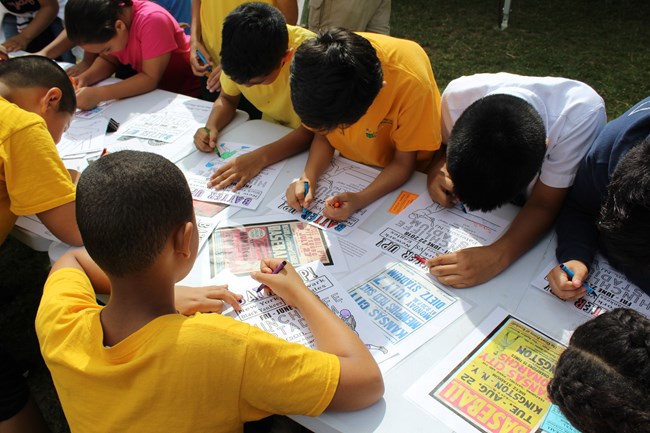 Children in yellow shirts standing at a table coloring baseball stadium activity sheets with crayons