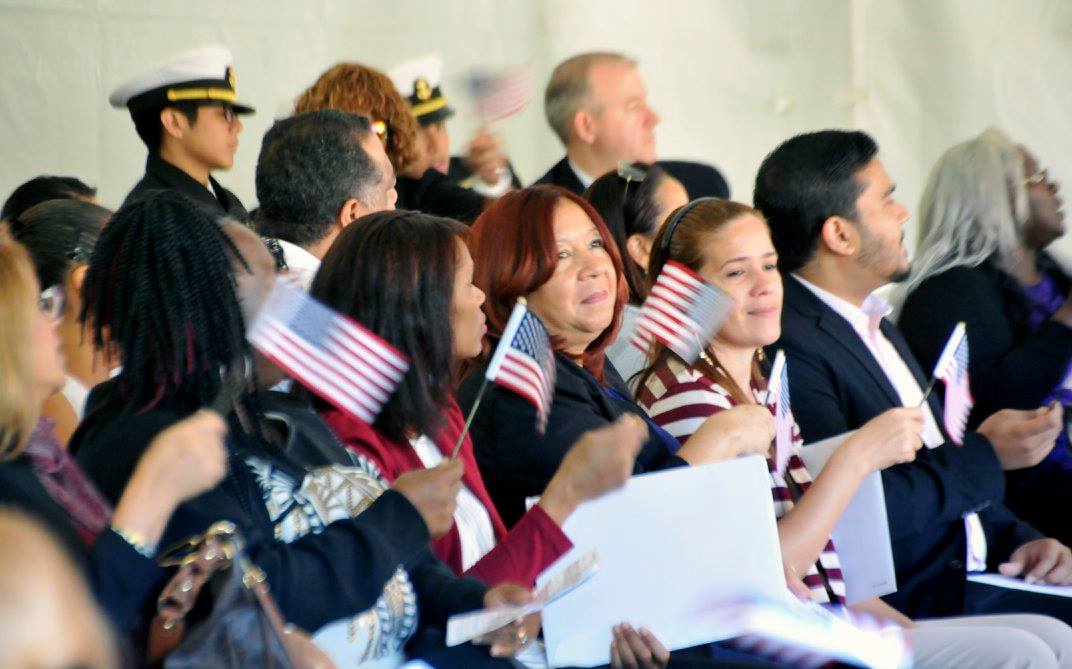 New U.S. citizens are smiling and waving American flags after taking the Oath of Allegiance. New citizens sworn in at Naturalization Ceremony