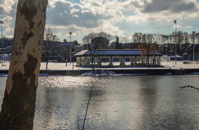A large pavilion & soccer field is seen from across the Passaic River, snow dusting the field & roof