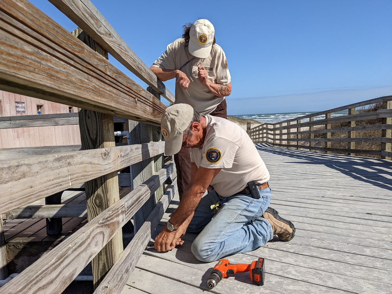Two volunteers fix a broken board on a boardwalk.