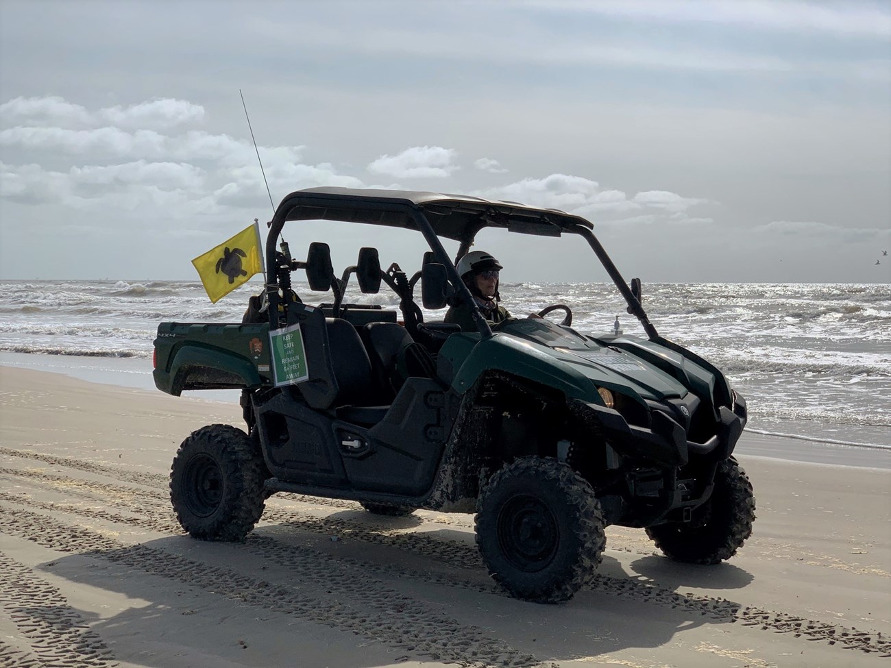 An UTV driving on the beach with a small bright yellow flag with a black silhouette of a sea turtle.