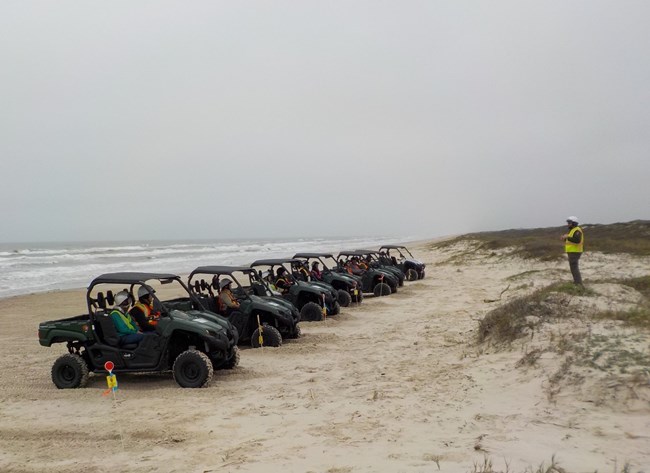Volunteers lined up in Utility Terrain Vehicles on the beach with an instructor teaching them.
