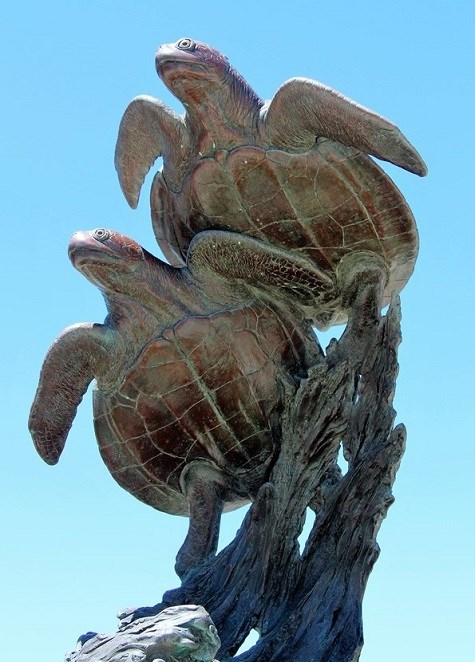 A bronze sculpture of two sea turtles swimming above a piece of drift wood.