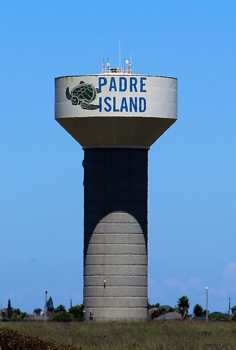 A light blue water tower with the following painted on the side, a green sea turtle along with large blue text that reads "Padre Island".
