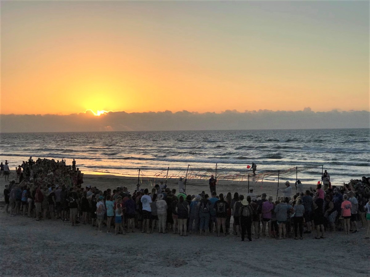 People gathered on the beach at dawn with the sun barely up and the ocean in the background.