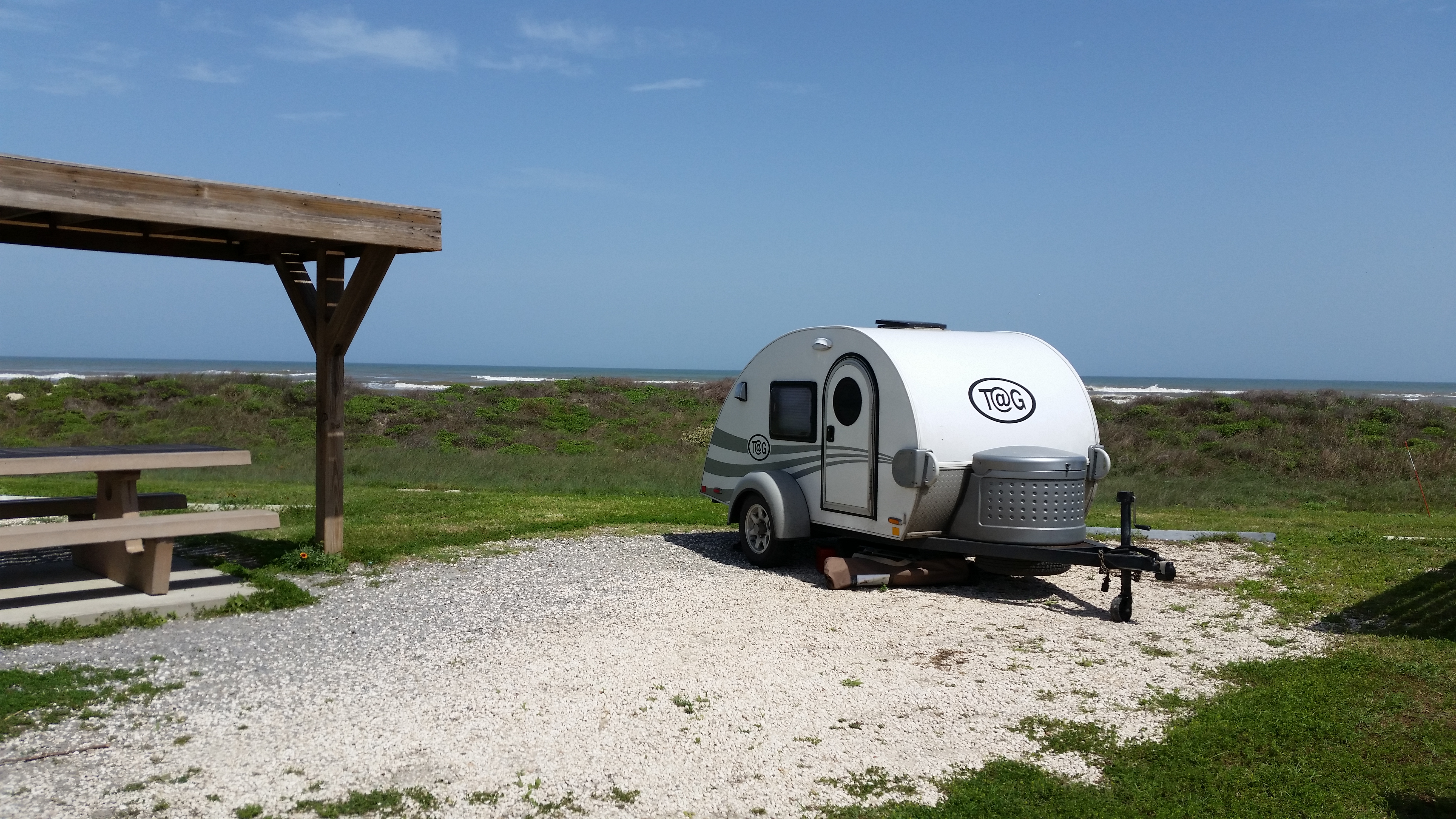 Campsite at Malaquite Campground Shade structure and picnic table on the left, a camper trailer on the right with the Gulf of Mexico in the background