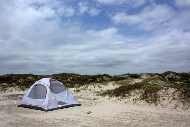 White Tent and Dunes Photo of a white tent on the beach with the dunes and a blue sky and clouds in the background.